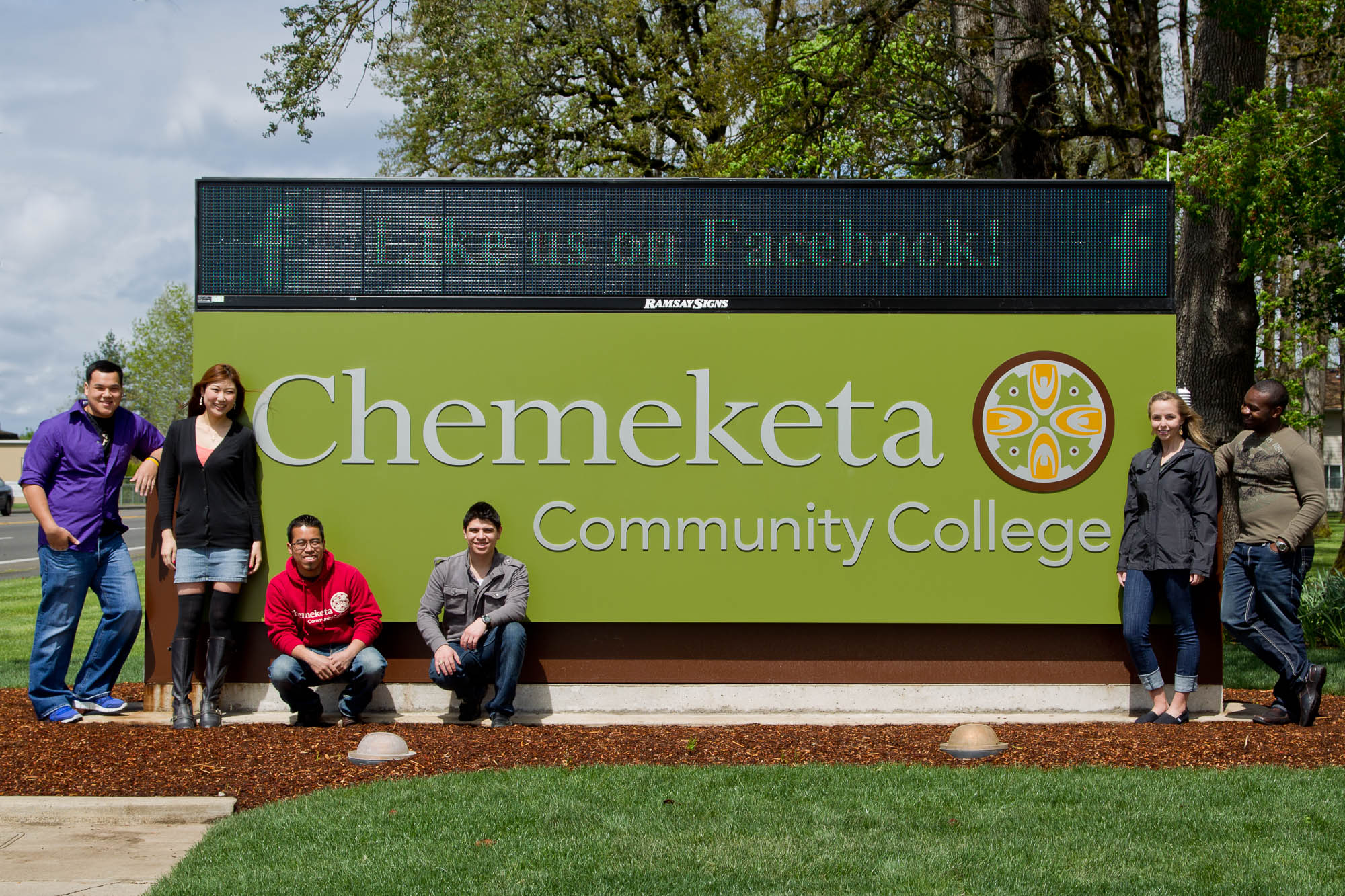 Student standing and sitting in front of the Chemeketa entrance sign at the Salem campus.