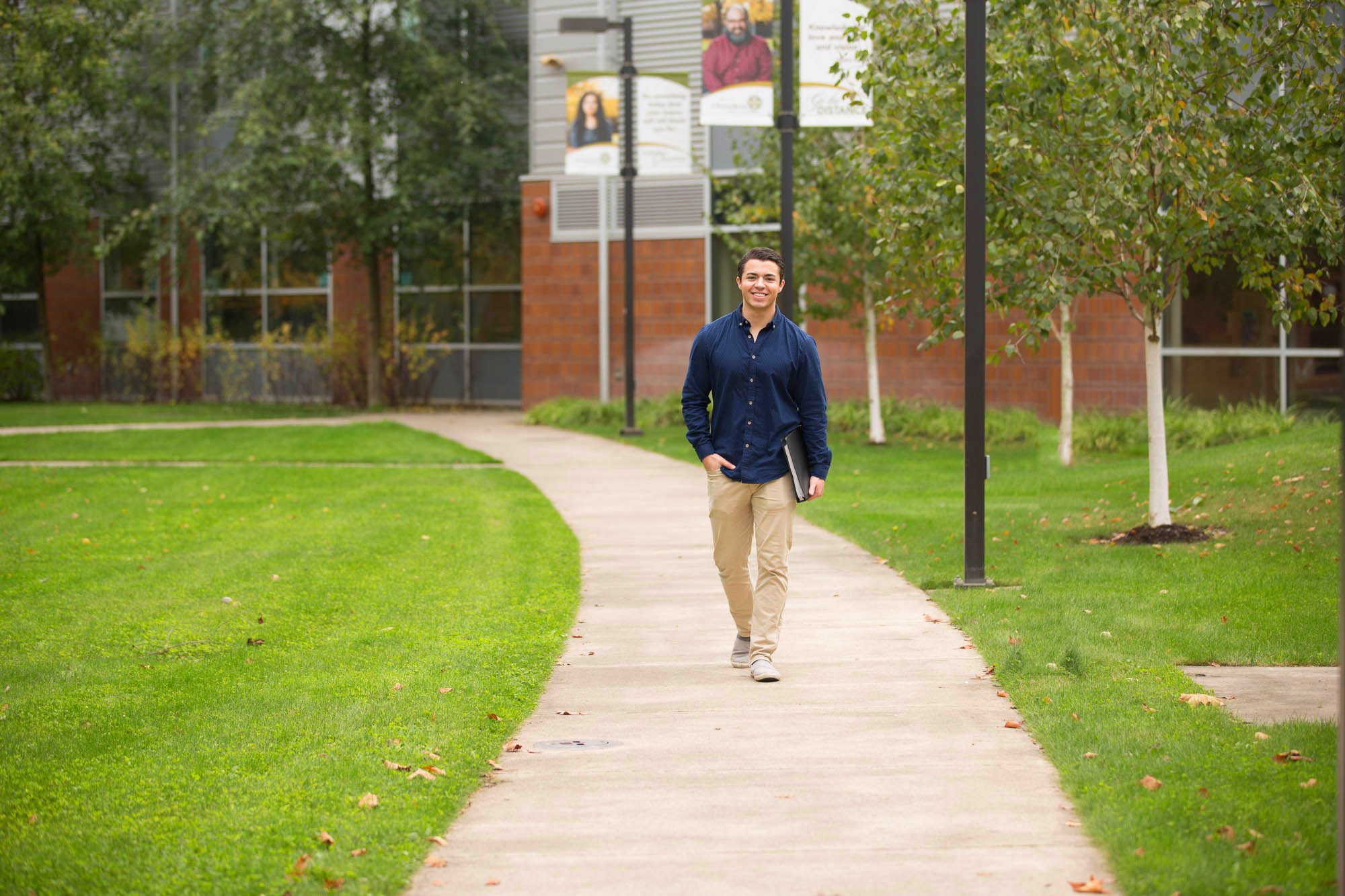 Male student walking down the sidewalk on the Salem campus carrying books in one hand.