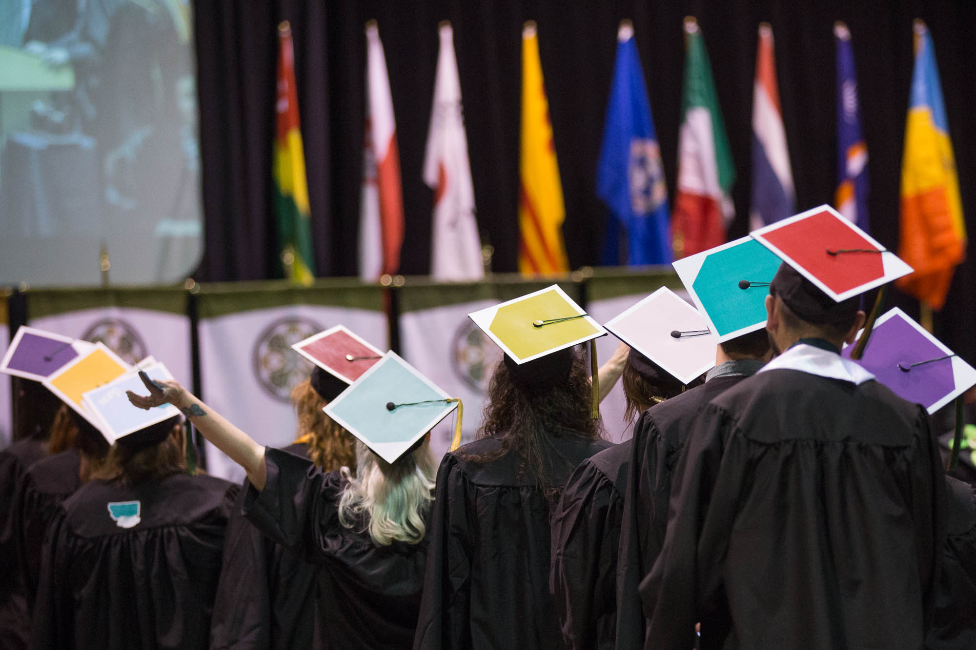 Students at a graduation ceremony wearing multi-color graduation caps.