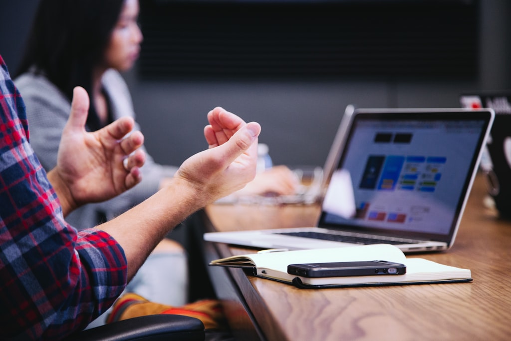 person sitting at table with laptop gesturing with hands